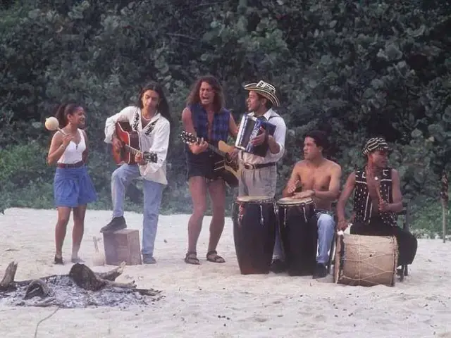 Grupo de músicos tocando en la playa con guitarras, acordeón y tambores.